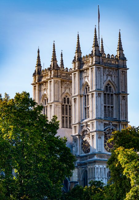 A detailed view of Westminster Abbey's Gothic architecture, featuring two prominent square towers with pointed spires and ornate stone carvings. The clock faces on the towers are visible, with one sho